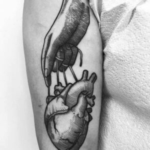 Das Tattoo ist eine Hand, die ein Herz hält, auf dem Oberarm platziert, symbolisiert Schutz und Liebe.